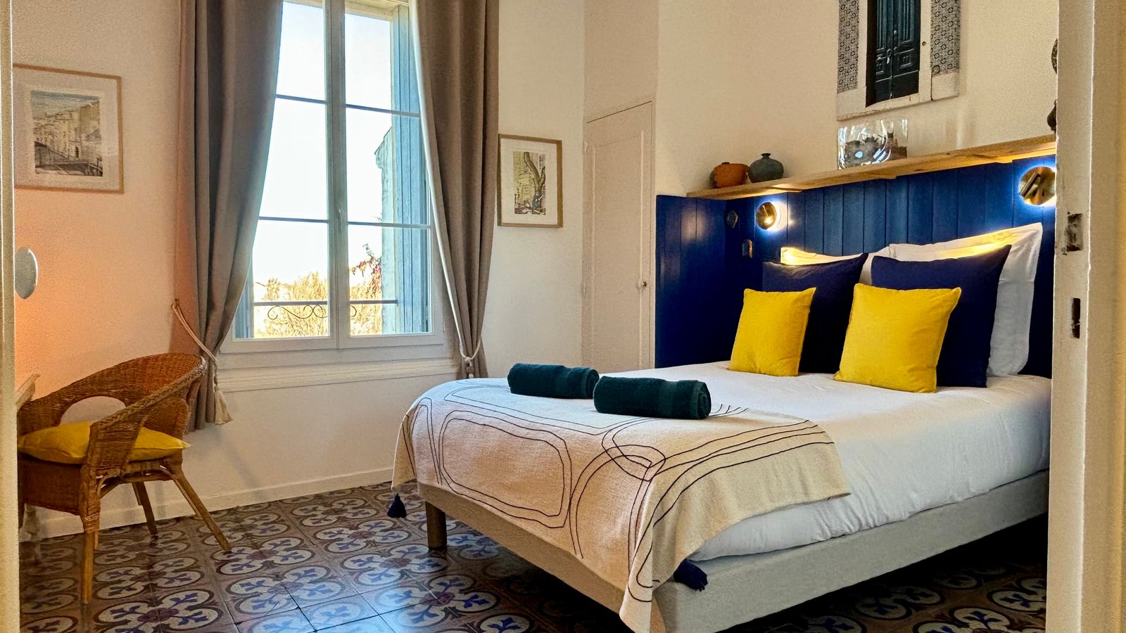 Intérieur d'une chambre aux draps jaune et bleu, une chaise en osier se trouve à côté du lit